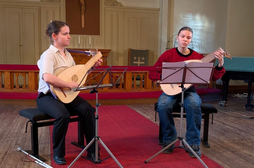 Kaksi naista vierekkäin tuoleilla soittamassa luuttuja, molempien edessä nuottiteline.